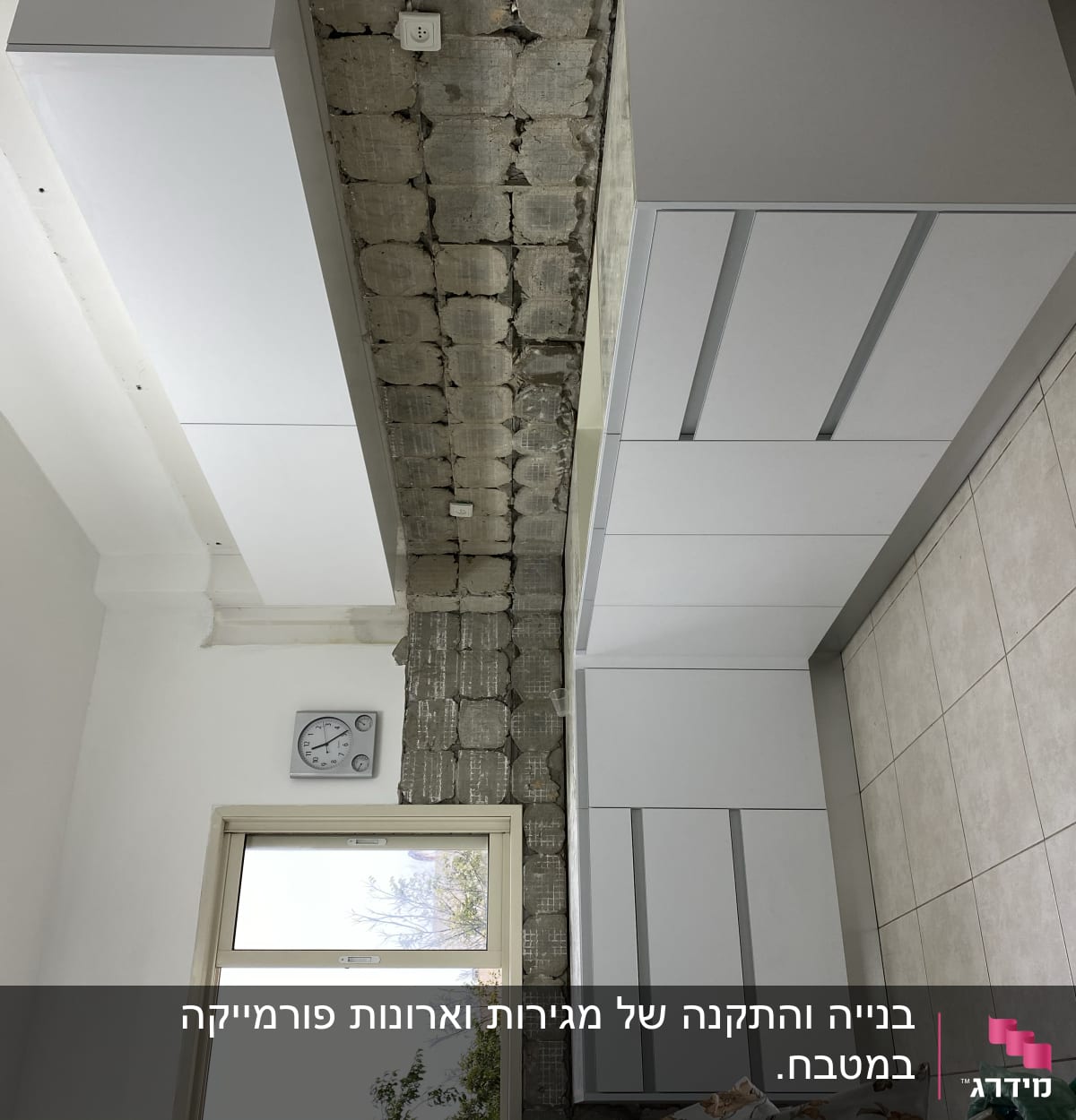 ארונות מטבח לבנים מותקנים על קיר בטון חשוף